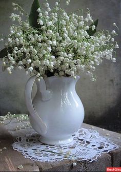 a white vase filled with flowers on top of a wooden table next to a lace doily