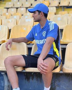 a man sitting on top of a wooden bench in front of a stadium filled with chairs