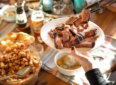 a person holding a plate with meat and potatoes on it next to other food dishes