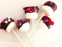 chocolate covered marshmallows with sprinkles and hearts on them sitting on a white surface