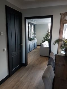 a living room filled with furniture next to a wooden floored hallway leading to a kitchen