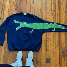 a blue sweater with a green alligator painted on it and white shoes next to it