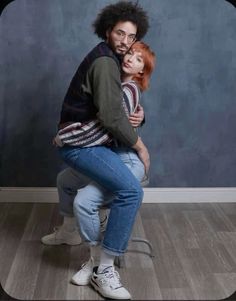 a man and woman hug each other while sitting on a stool in front of a blue wall