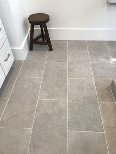 a bathroom with gray tile and white cabinets in it, along with a stool on the floor