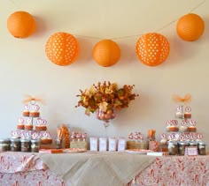 an orange and white dessert table set up with paper lanterns, candy bars, and candies