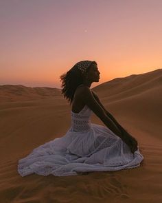 a woman sitting in the desert at sunset