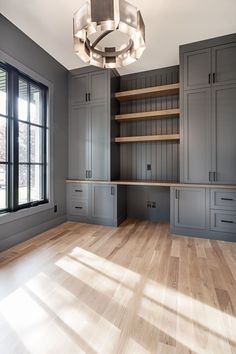 an empty room with wooden floors and gray cabinets, including a chandelier hanging from the ceiling