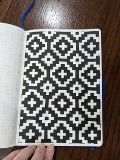 an open book with black and white designs on it, being held by someone's hand