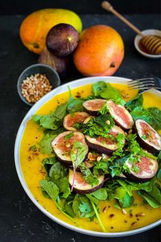 a plate filled with figs and greens on top of a table next to other fruits