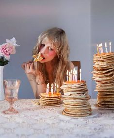 a woman sitting at a table with stacks of pancakes and lit candles in front of her