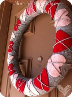 a red and white wreath is hanging on the front door with yarn wrapped around it