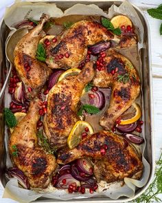 chicken with lemons, onions and herbs in a baking dish on a white wooden table