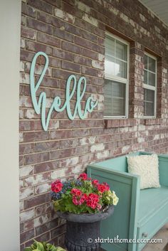 a blue bench sitting in front of a brick building with flowers on the ground and a sign that says hello