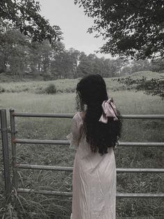 a woman standing in front of a fence looking over the top of her head at an open field