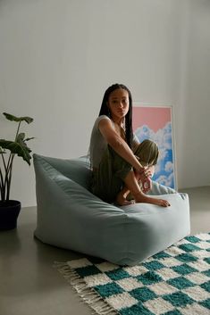 a woman sitting on top of a bean bag chair next to a potted plant