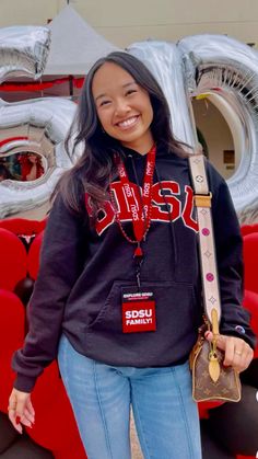 a woman standing in front of some red seats holding a baseball bat and smiling at the camera