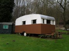 an old trailer sits in the middle of a grassy area with trees and other things around it