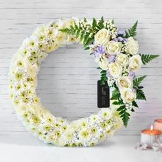 a wreath with white flowers and greenery next to candles