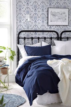 a bed with blue and white sheets in a bedroom next to a potted plant