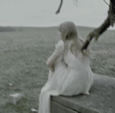 a woman in a white dress is sitting on a wall and looking at the ground