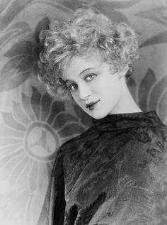 black and white photograph of a woman with curly hair wearing a dress in front of a floral wallpaper