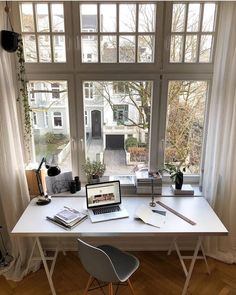 a laptop computer sitting on top of a white desk in front of a large window