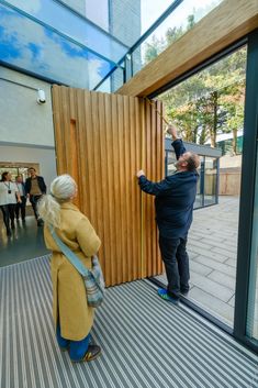 A timber entrance door in a glass wall with a person measuring the door shown open Solid Front Door, Timber Entrance, Entrance Design, Entrance Door, Entrance Doors, New Builds, Glass Wall, Windows And Doors