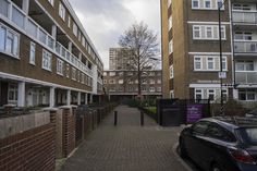 cars parked on the side of a brick road next to tall buildings with balconies