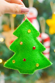 a hand holding a green felt christmas tree ornament in front of a christmas tree