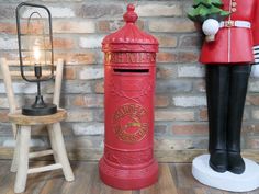 a red mailbox sitting next to a wooden chair and table with a lamp on it