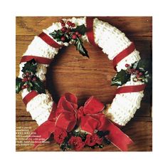 a crocheted christmas wreath with holly and red ribbon on a wooden table top