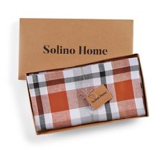 an open box with a tag on it next to a brown and white checkered shirt