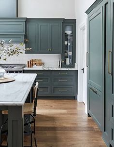 a kitchen with green cabinets and white marble counter tops, along with wooden flooring