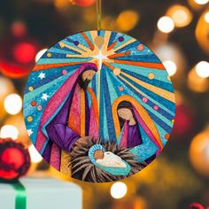 an ornament hanging from a christmas tree with lights in the background and a nativity scene on it