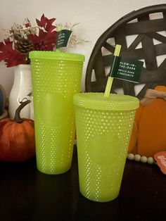 two green cups sitting on top of a table next to pumpkins and other decorations