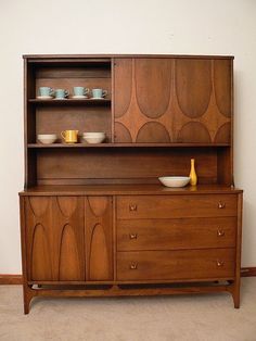 a wooden cabinet with bowls and cups on it's top, against a white wall