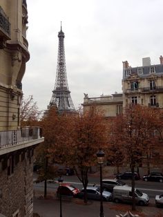 the eiffel tower is in the distance, with cars parked on the street