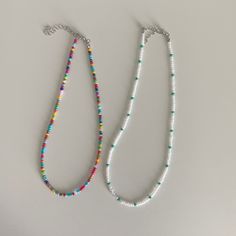 two necklaces with different colored beads and silver chains on a white surface, one beaded