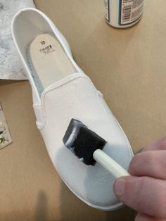 a person painting a pair of white shoes with a black paintbrush on the sole