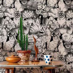 a table topped with a potted plant next to a wall covered in cats