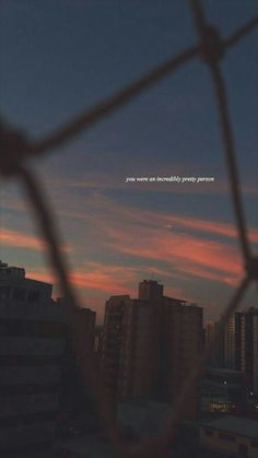 the sky is pink and blue as seen through a chain link fence with buildings in the background