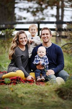 a man, woman and child sitting on a blanket in the grass with trees behind them