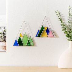 two geometric stained glass pieces hanging on a wall next to a vase with a plant in it