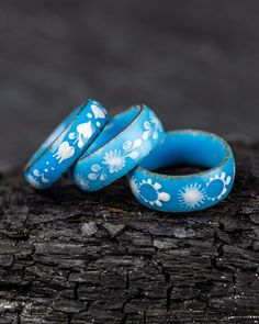 two blue rings sitting on top of a piece of wood next to another ring with white flowers