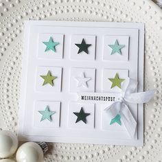 a white card with green and silver stars on it, tied in a bow next to some ornaments