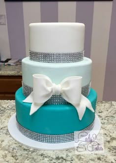 a three tiered cake with blue and white frosting, decorated with bowknots