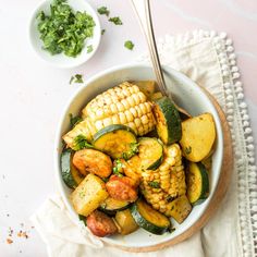 a bowl filled with corn and vegetables on top of a white cloth next to a spoon