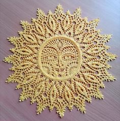 a crocheted doily with a face in the center on a wooden surface