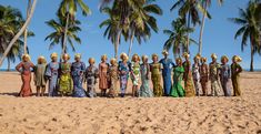 a group of women standing on top of a sandy beach next to palm tree covered trees