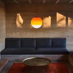 a couch and table in a room with concrete walls, red rugs and large round light fixture